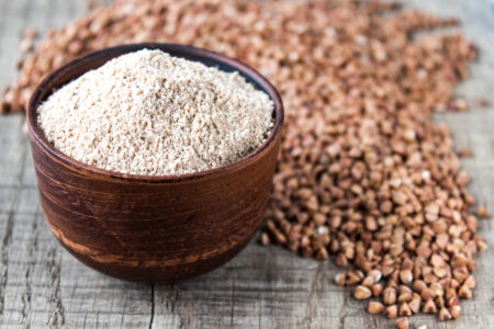 Buckwheat flour in a bowl near the buckwheat grain. A pile of buckwheat flour. Close-up.